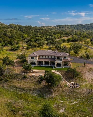 Stone villa with terracotta roof on hillside surrounded by oak trees and rolling countryside